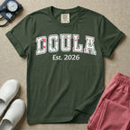 A personalized Doula graphic featuring the word DOULA in large, arched varsity-style letters filled with a delicate pink and green floral pattern, positioned above customizable text that reads Est. 2026.
