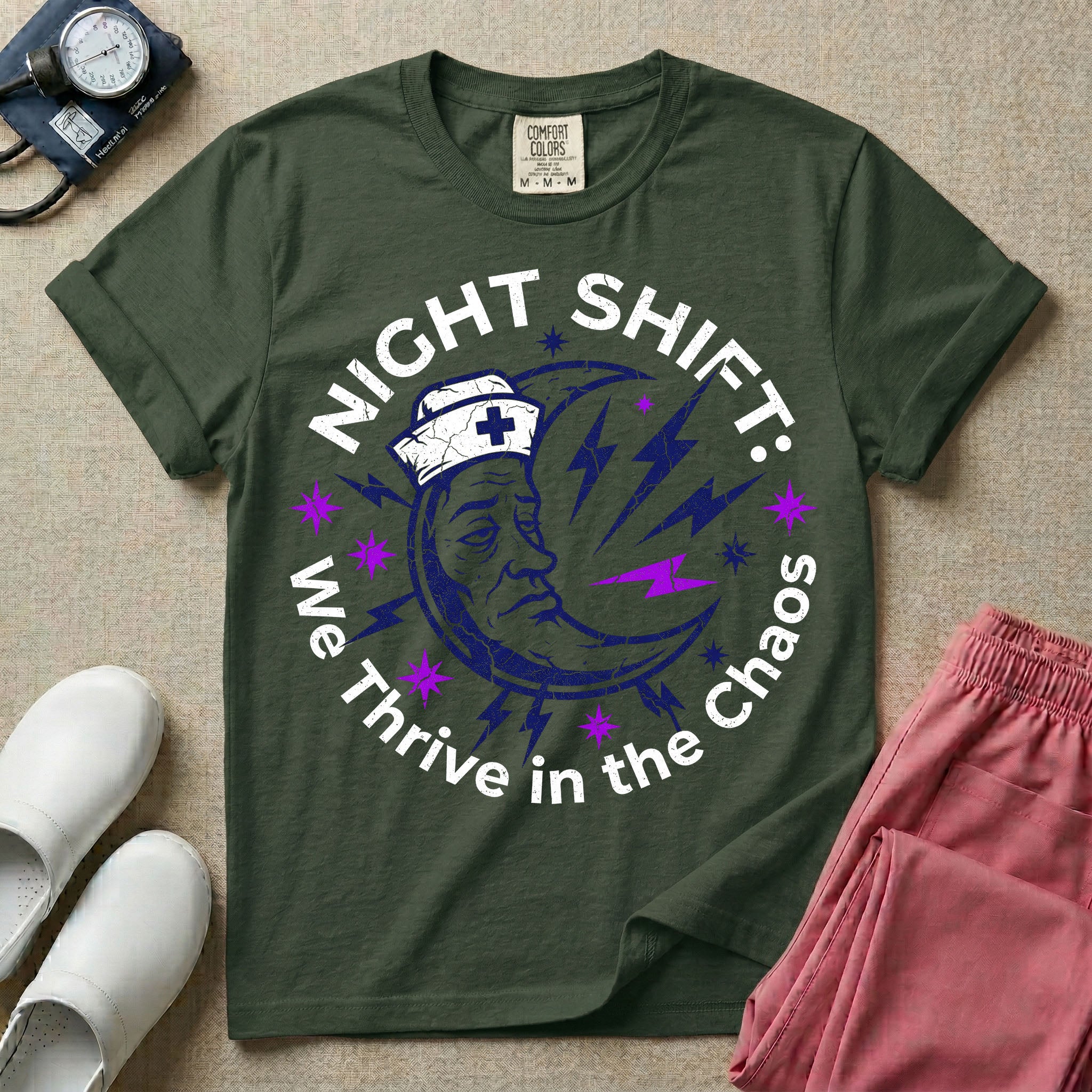 General nursing night shift nurse t-shirt with a retro purple moon wearing a nurse cap and we thrive in the chaos graphic in moss color.