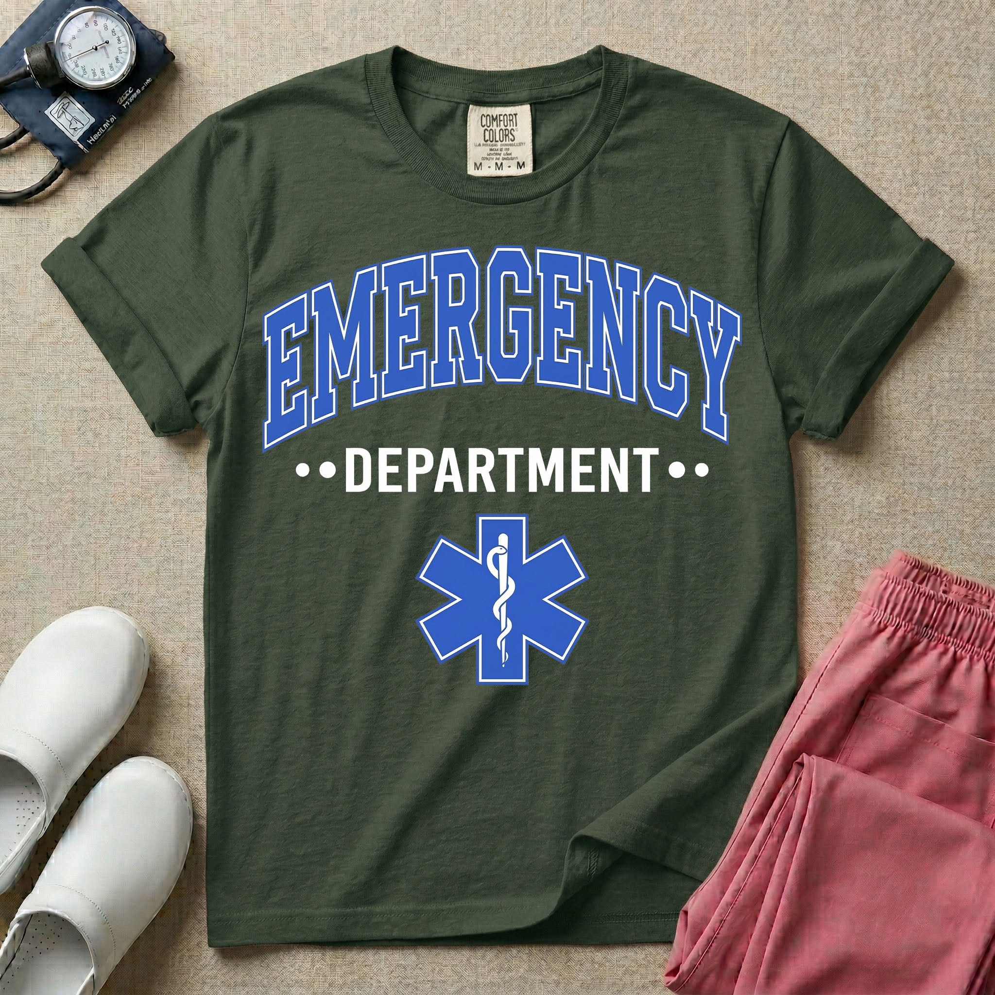 A classic varsity-style t-shirt for emergency room nurses featuring the word "EMERGENCY" in a large, arched blue collegiate font above the word "DEPARTMENT", centered over a blue Star of Life medical symbol.