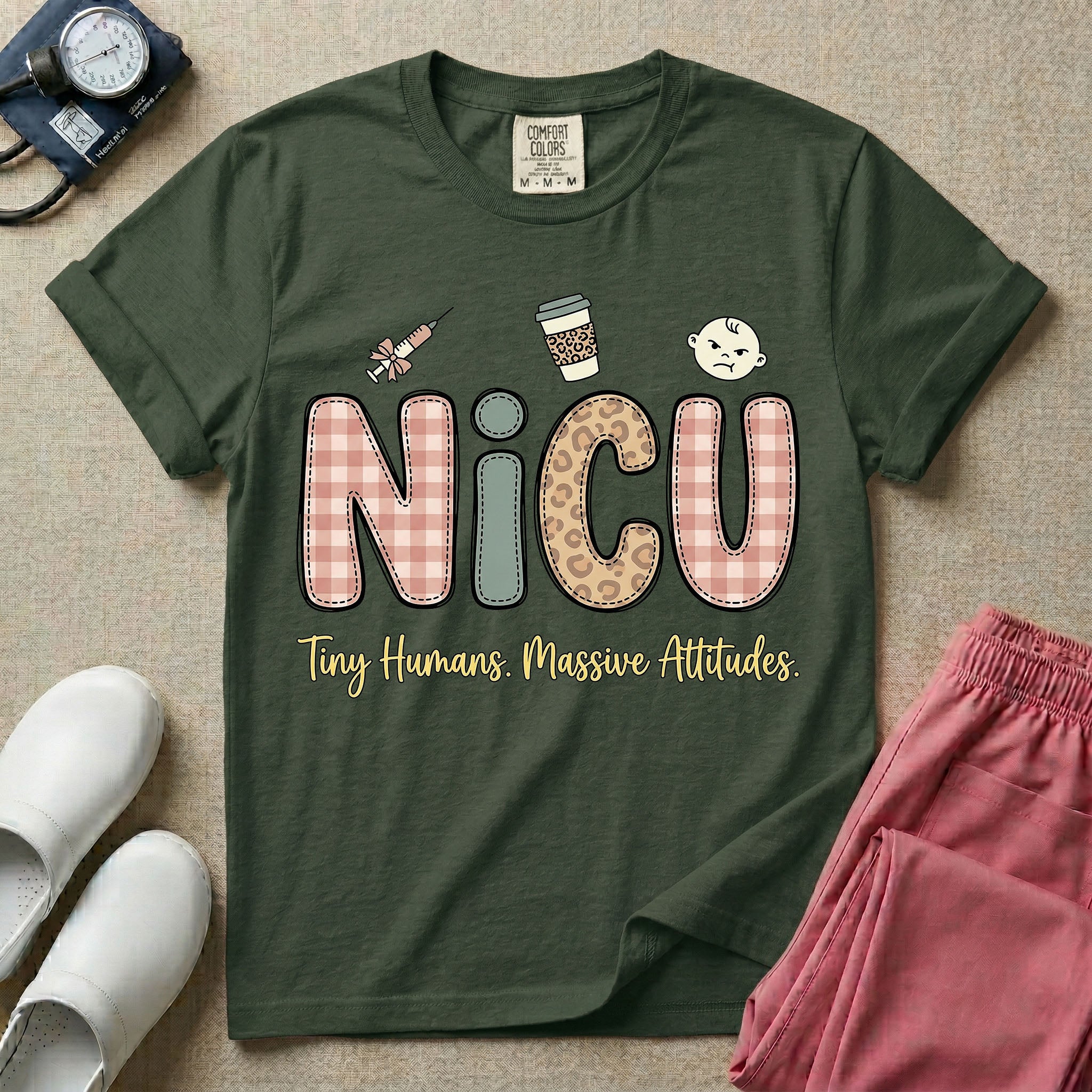 A humorous t-shirt for NICU nurses featuring the large text "NICU" in plaid and patterned letters with the phrase "Tiny Humans. Massive Attitudes." underneath, accompanied by small cute graphics of a syringe, an iced coffee cup, and a baby's face.