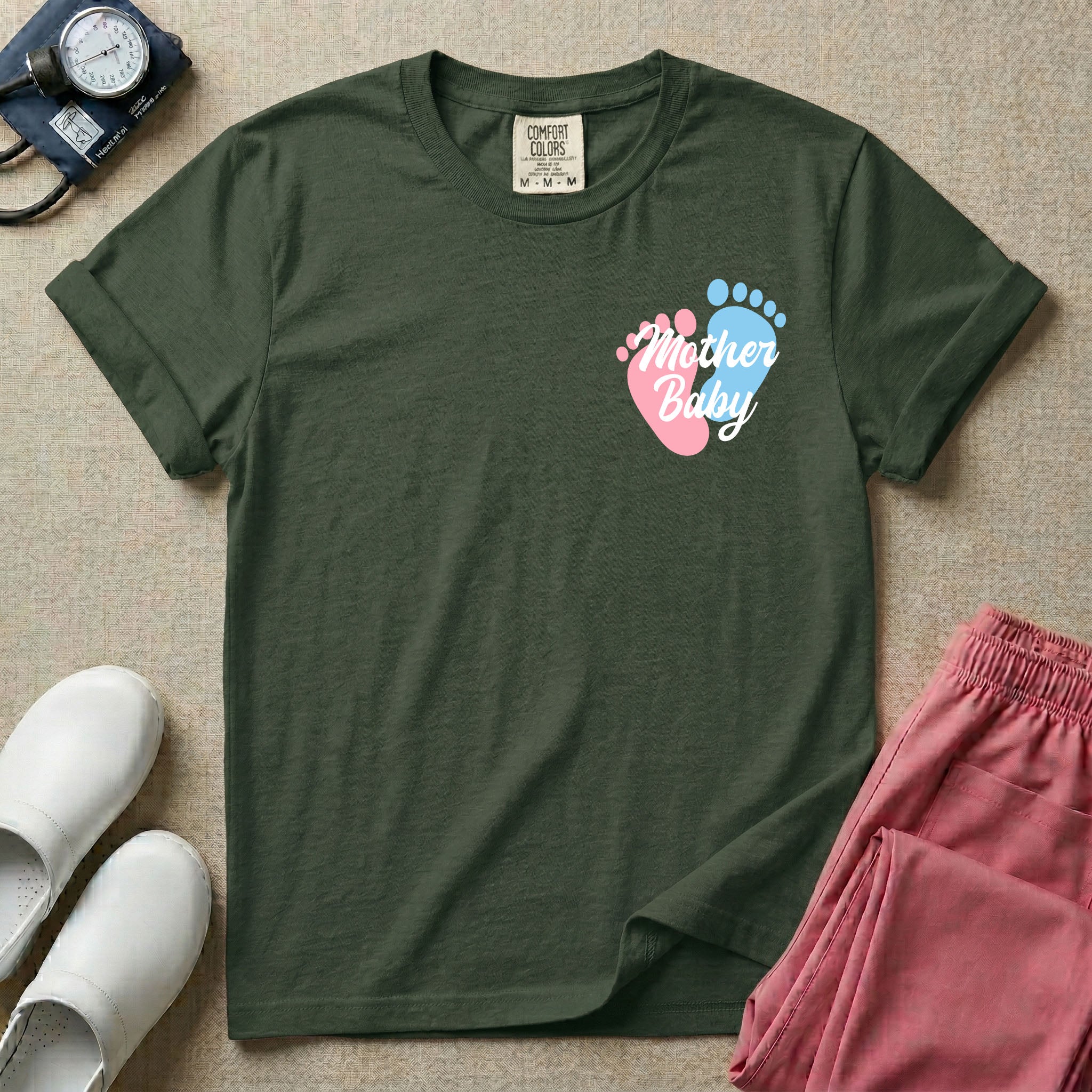 A minimalist postpartum nursing t-shirt featuring a small left chest graphic of two baby footprints, one pink and one blue, with the cursive white text "Mother Baby" written across them.