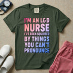 A humorous graphic tee for labor and delivery nurses featuring bold, gradient block lettering that reads "I'M AN L&D NURSE I'VE BEEN SQUIRTED BY THINGS YOU CAN'T PRONOUNCE".