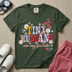 A t-shirt featuring the text Tiny Humans are my favorite in colorful retro bubble letters decorated with daisies, sparkles, and red hearts with a small NICU heart logo at the bottom.