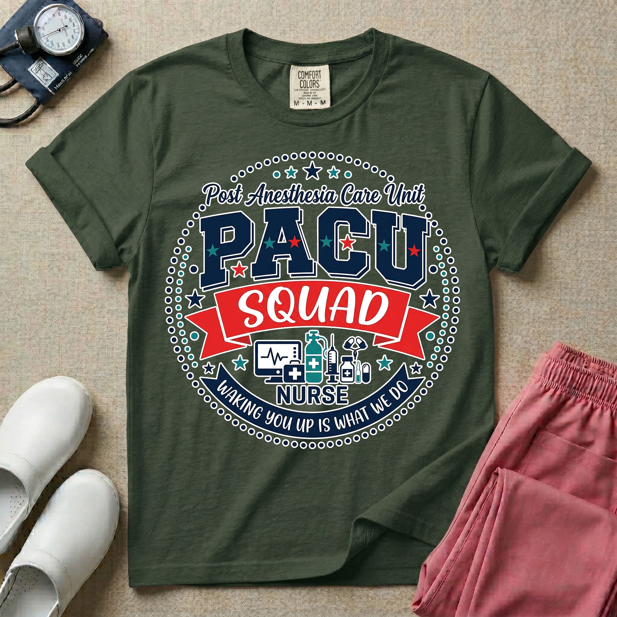 A t-shirt featuring a circular badge design with the text PACU SQUAD in block letters, medical icons like a heart monitor and stethoscope, and the phrase Waking You Up Is What We Do.