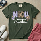 A funny t-shirt for NICU nurses featuring the text "NICU I Work for a 4-Pound Dictator" designed with purple plaid and leopard print letters, accompanied by graphics of a baby bottle with a bow and a rattle that says "WARNING: TINY BOSS".