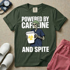 A humorous graphic for general nursing featuring an illustration of a skeleton wearing a green scrub cap and dark blue scrubs, holding a large white coffee cup with a yellow biohazard symbol, with the stacked text 'POWERED BY CAFFEINE' above it and 'AND SPITE' below it.