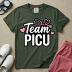 A descriptive graphic tee for pediatric intensive care nurses featuring the text "Team PICU" in bold white lettering, accented with pink hearts and a pink stethoscope design.