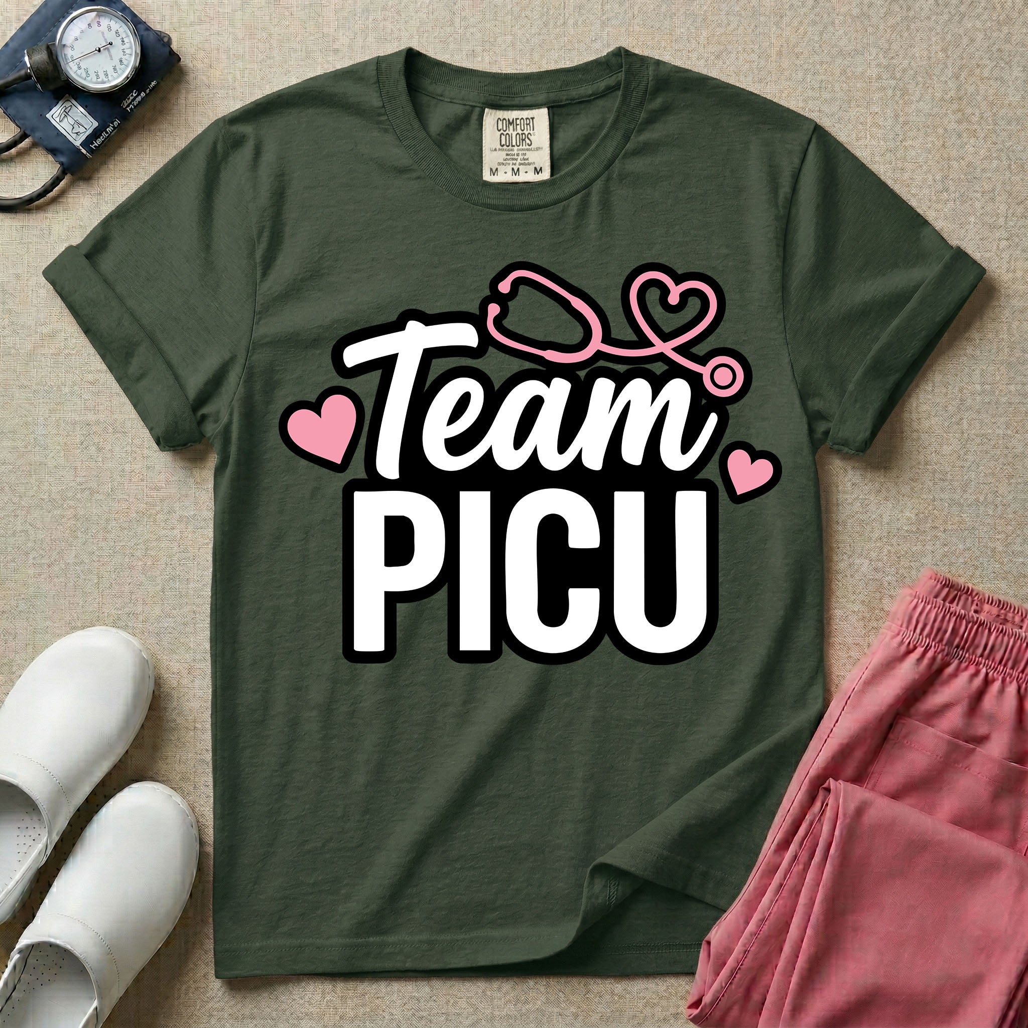 A descriptive graphic tee for pediatric intensive care nurses featuring the text "Team PICU" in bold white lettering, accented with pink hearts and a pink stethoscope design.