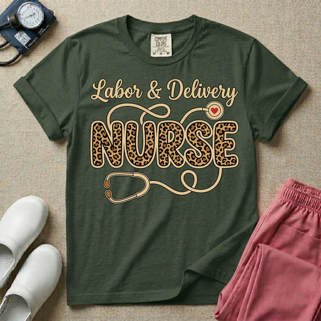 A graphic t-shirt for a Labor and Delivery unit featuring the text 'Labor & Delivery' in beige script above the word 'NURSE' in large leopard print letters, intertwined with an illustration of a stethoscope that features a small red heart on the chest piece.