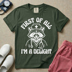 A humorous graphic of a raccoon dressed in a nursing cap and scrub jacket with a stethoscope, with the text "FIRST OF ALL I'M A DELIGHT", in moss color.