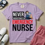A retro ER nursing t-shirt featuring the bold text "NEVER UNDERESTIMATE AN EMERGENCY NURSE" alongside a vintage graphic of a masked nurse flexing her arm in a classic Rosie the Riveter pose
