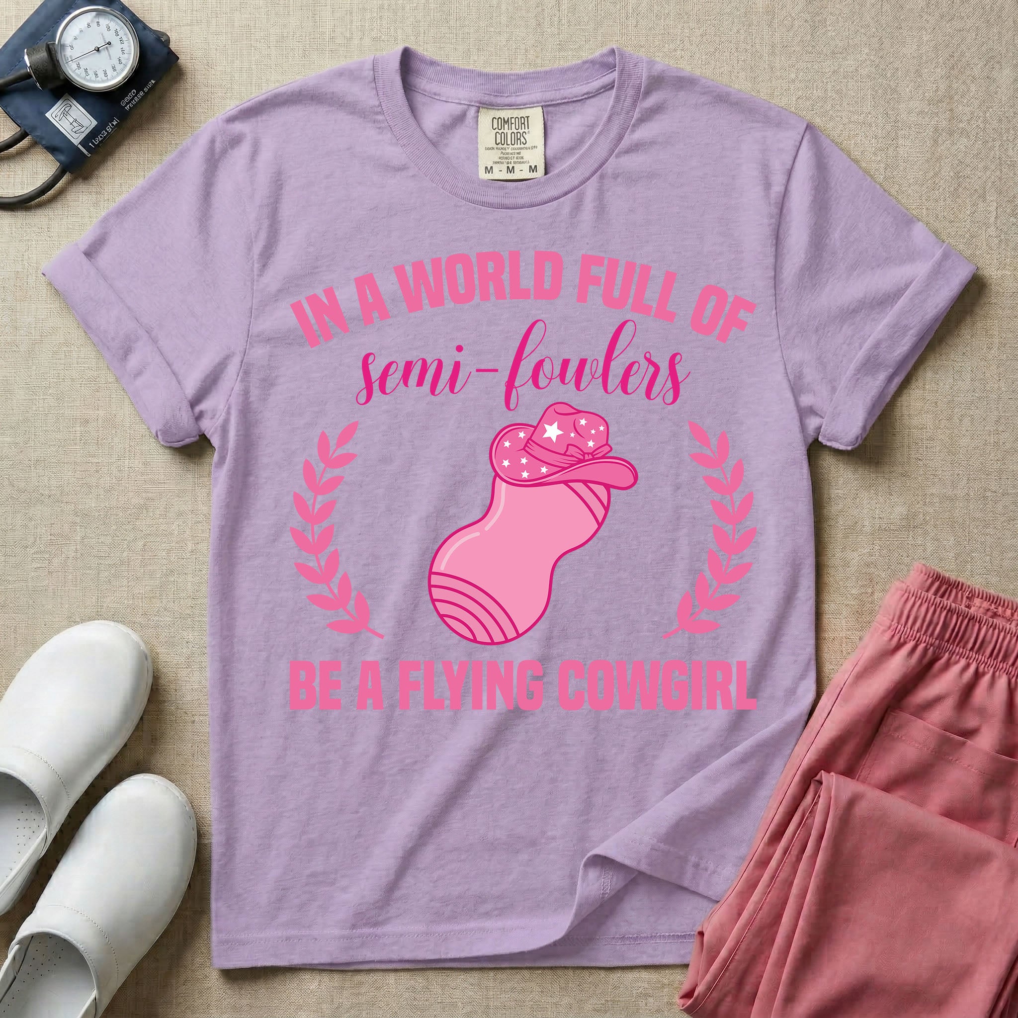 A humorous graphic tee for labor and delivery nurses featuring an illustration of a peanut ball wearing a cowboy hat, framed by laurel branches, along with the text "IN A WORLD FULL OF semi-fowlers BE A FLYING COWGIRL".