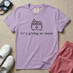 A funny minimalist ER nursing t-shirt featuring a simple white line drawing of a dumpster on fire with a medical cross on it, sitting above the lower-case typewriter text "it's giving er nurse".