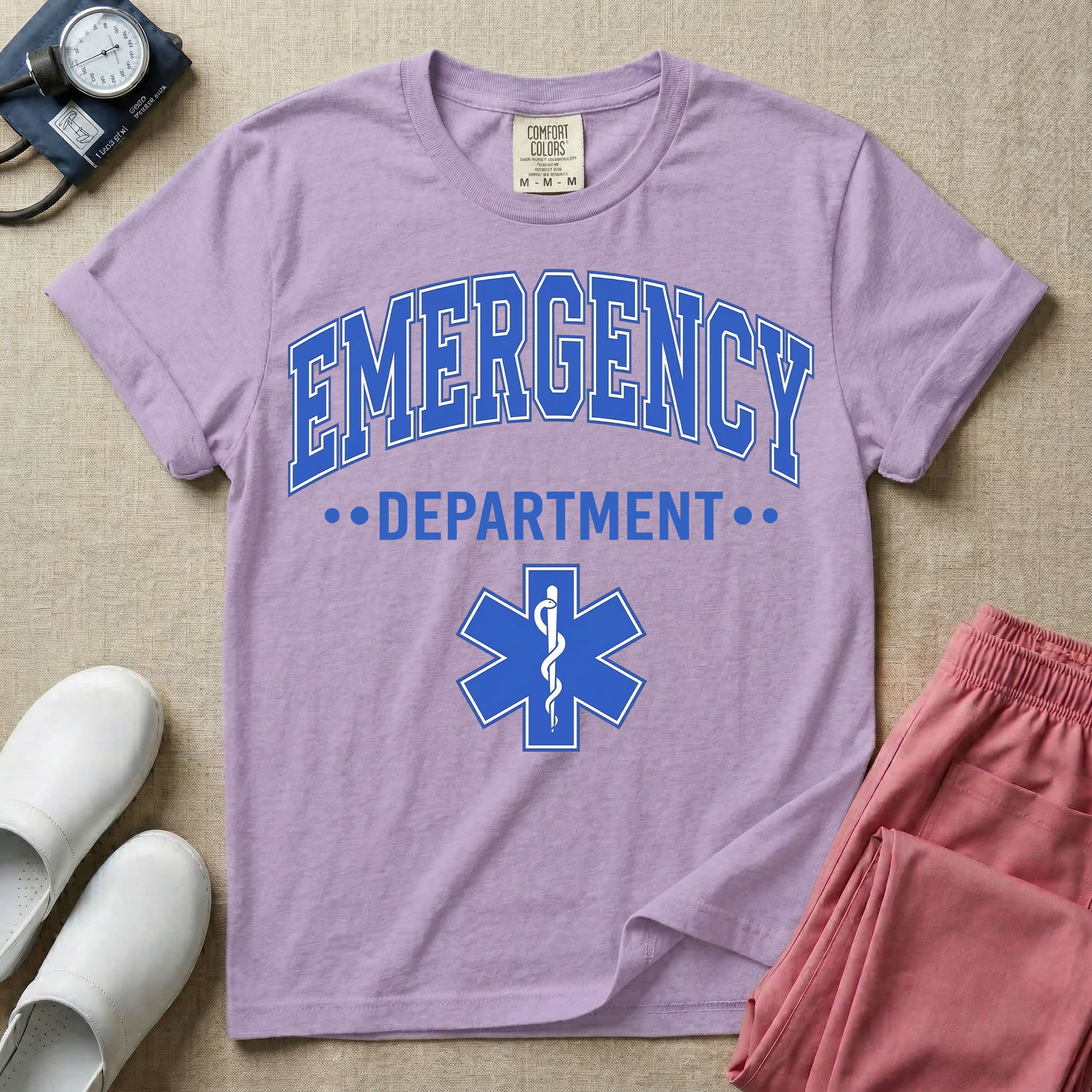 A classic varsity-style t-shirt for emergency room nurses featuring the word "EMERGENCY" in a large, arched blue collegiate font above the word "DEPARTMENT", centered over a blue Star of Life medical symbol.