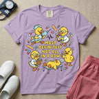 General nursing t-shirt featuring a chaotic group of cartoon ducklings dressed as medical professionals with the text "MOST DEFINITELY NOT ALL IN A ROW" on a sage green garment, in orchid color.