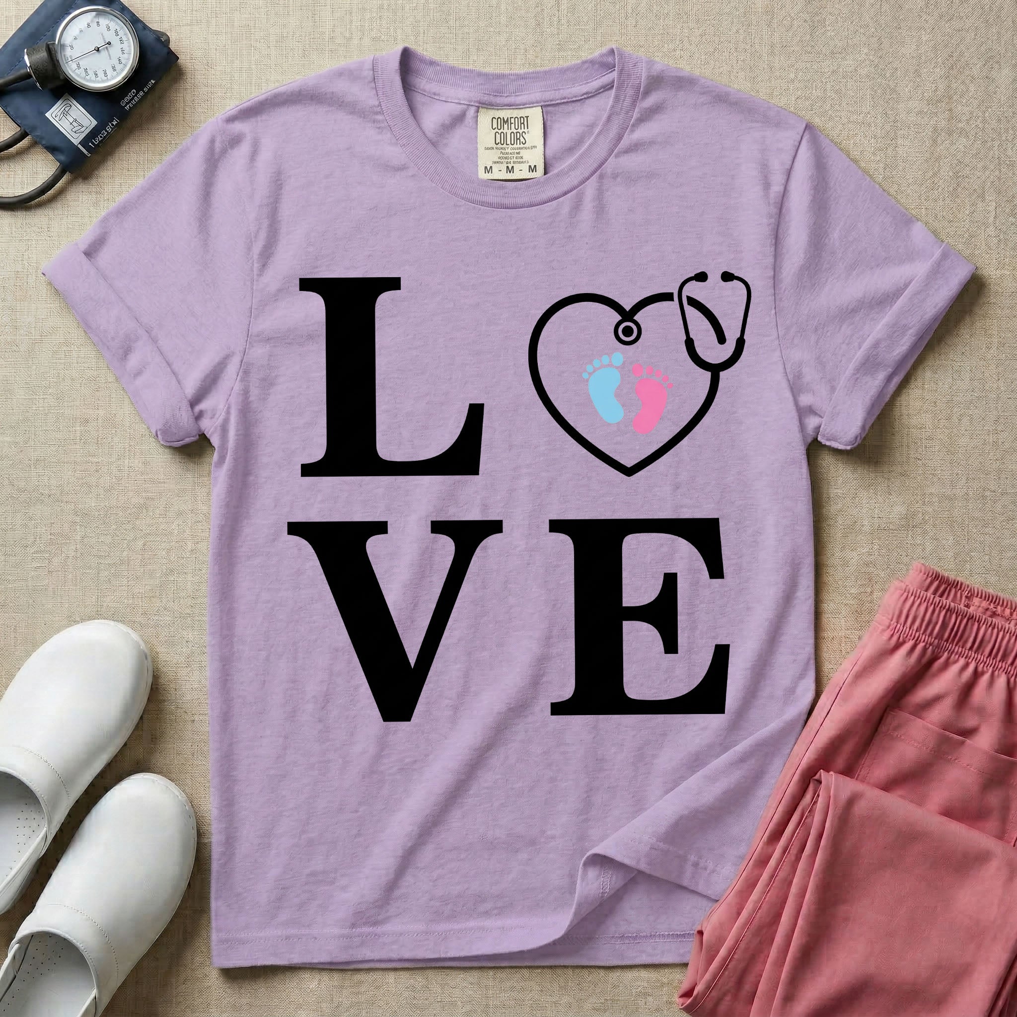 A minimalist nursing t-shirt featuring the word LOVE stacked in large white serif letters, with the letter O replaced by a white stethoscope shaped like a heart containing two small baby footprints, one pink and one blue.