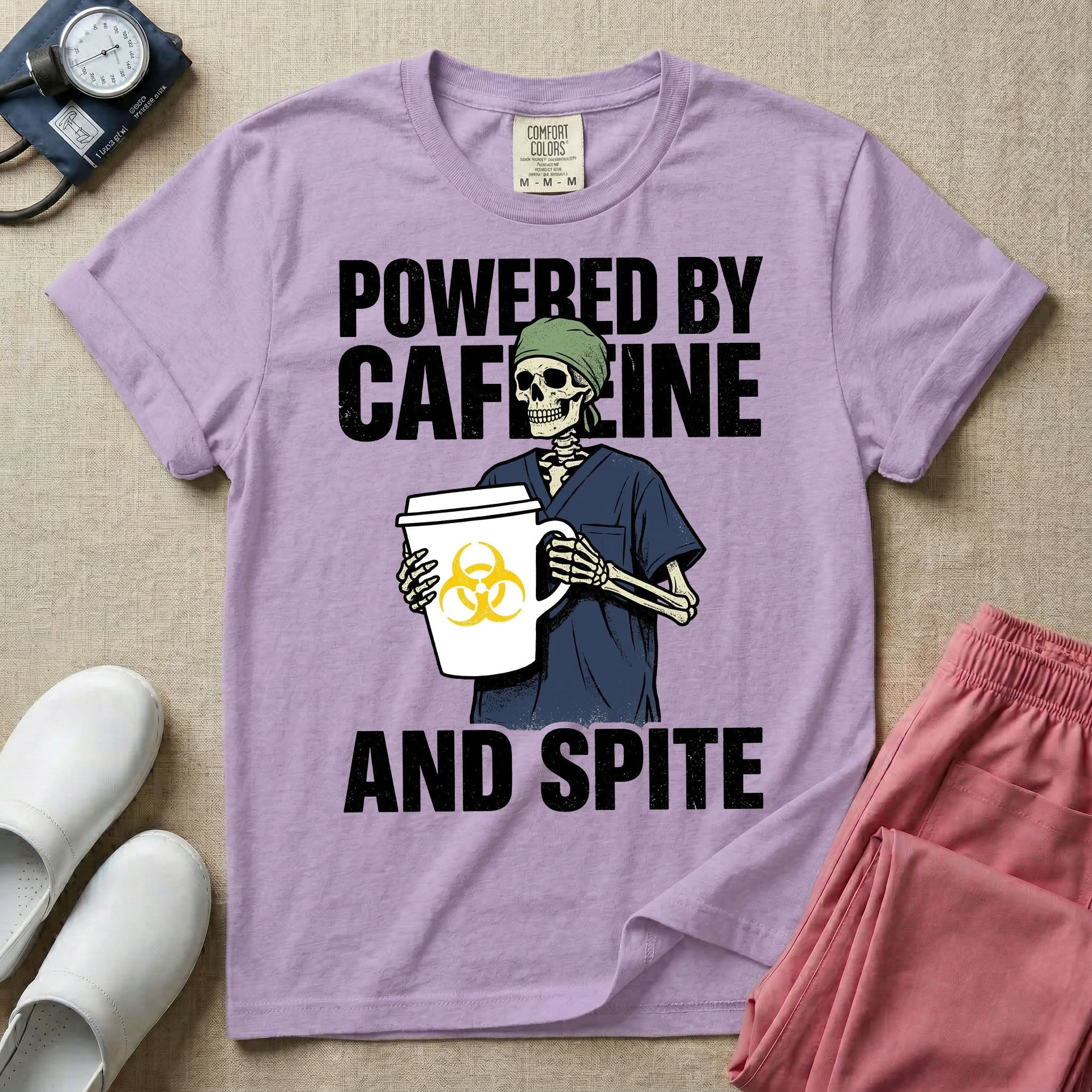 A humorous graphic for general nursing featuring an illustration of a skeleton wearing a green scrub cap and dark blue scrubs, holding a large white coffee cup with a yellow biohazard symbol, with the stacked text 'POWERED BY CAFFEINE' above it and 'AND SPITE' below it.