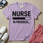 General nursing student t-shirt featuring a white loading bar graphic and the text "NURSE IN PROGRESS..." on a dark gray garment, in orchid color.