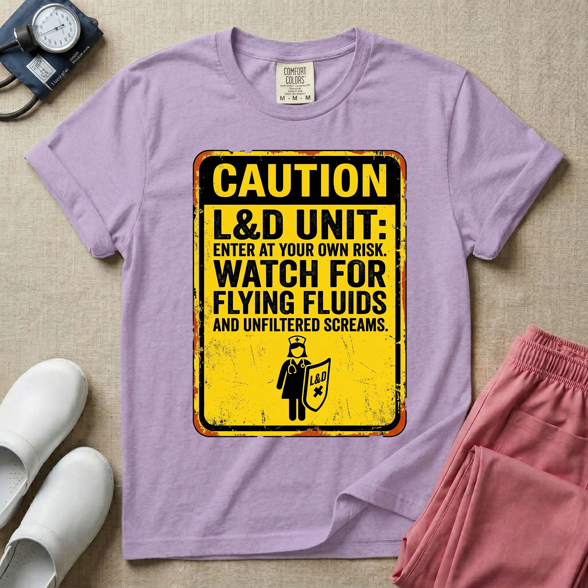 A humorous graphic tee for labor and delivery nurses featuring a distressed caution sign design with the text "CAUTION L&D UNIT: ENTER AT YOUR OWN RISK. WATCH FOR FLYING FLUIDS AND UNFILTERED SCREAMS." above a stick figure nurse holding a shield.