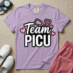 A descriptive graphic tee for pediatric intensive care nurses featuring the text "Team PICU" in bold white lettering, accented with pink hearts and a pink stethoscope design.