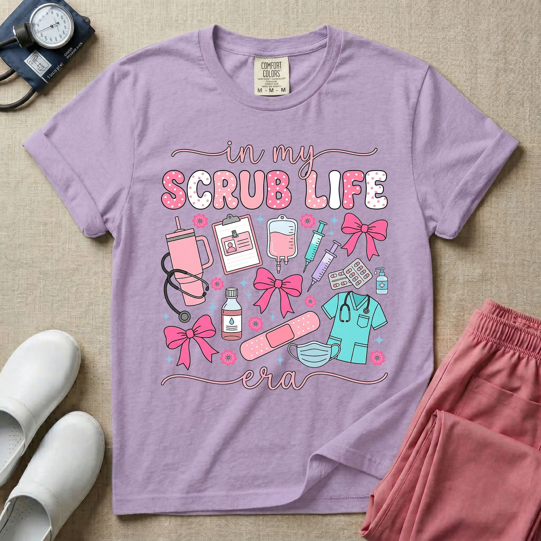 A cute general nursing t-shirt featuring the retro text "in my SCRUB LIFE era" surrounded by coquette medical graphics including a pink tumbler cup, stethoscope, IV bag with pink bows, clipboard, and blue scrubs.