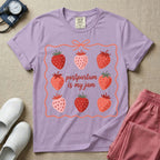 A funny and cute postpartum nursing t-shirt featuring the pun text "postpartum is my jam" surrounded by a graphic of red and pink strawberries, enclosed in a decorative wavy border with a bow at the top.