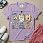 A retro-style t-shirt for emergency room nurses featuring the text "ER CREW" below a vintage cartoon illustration of a medicine bottle, a grumpy clipboard holding an AMA form, and a sandwich wearing a nurse cap walking together.