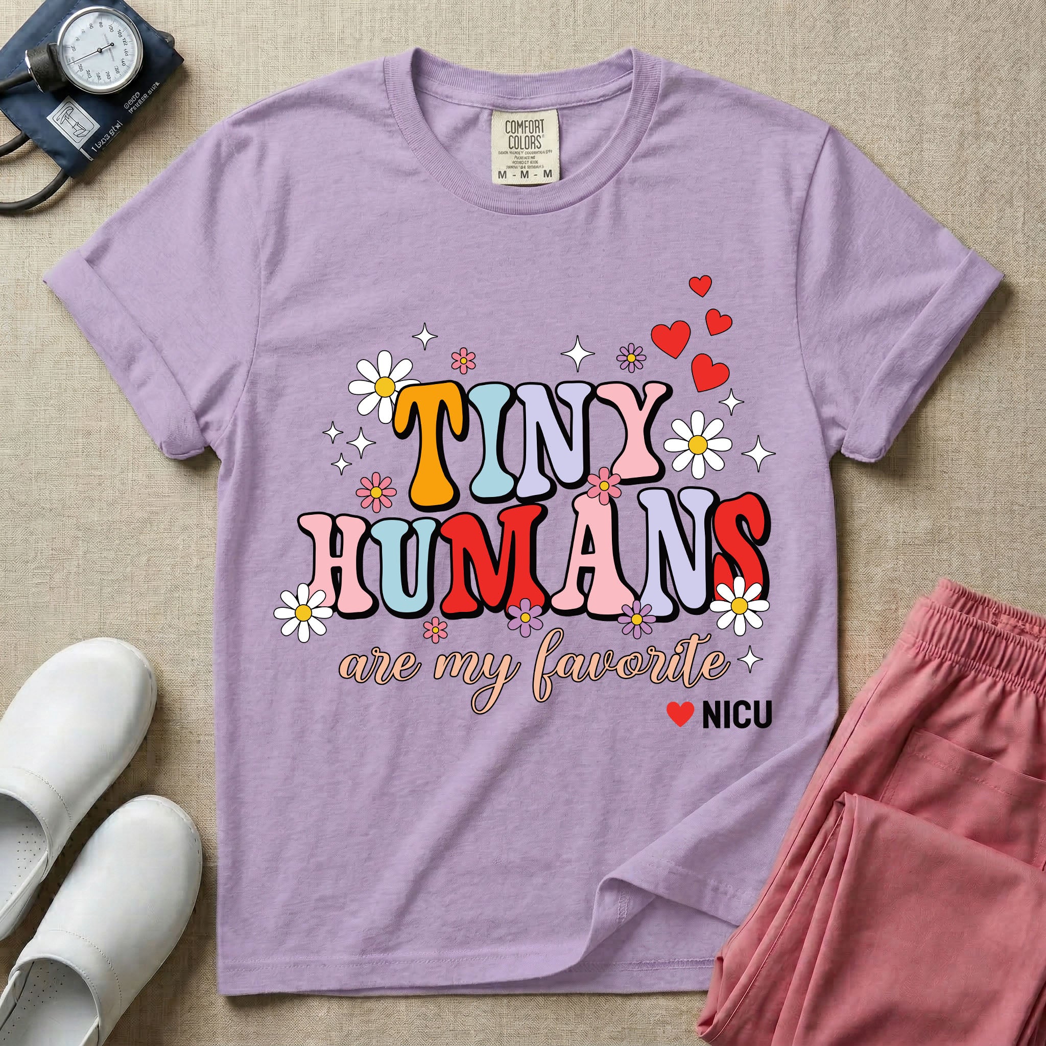 A t-shirt featuring the text Tiny Humans are my favorite in colorful retro bubble letters decorated with daisies, sparkles, and red hearts with a small NICU heart logo at the bottom.