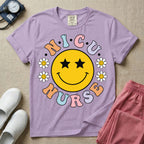 A t-shirt featuring a large yellow smiley face with star eyes surrounded by smiley face daisies and the text N.I.C.U. NURSE in pastel retro bubble lettering.