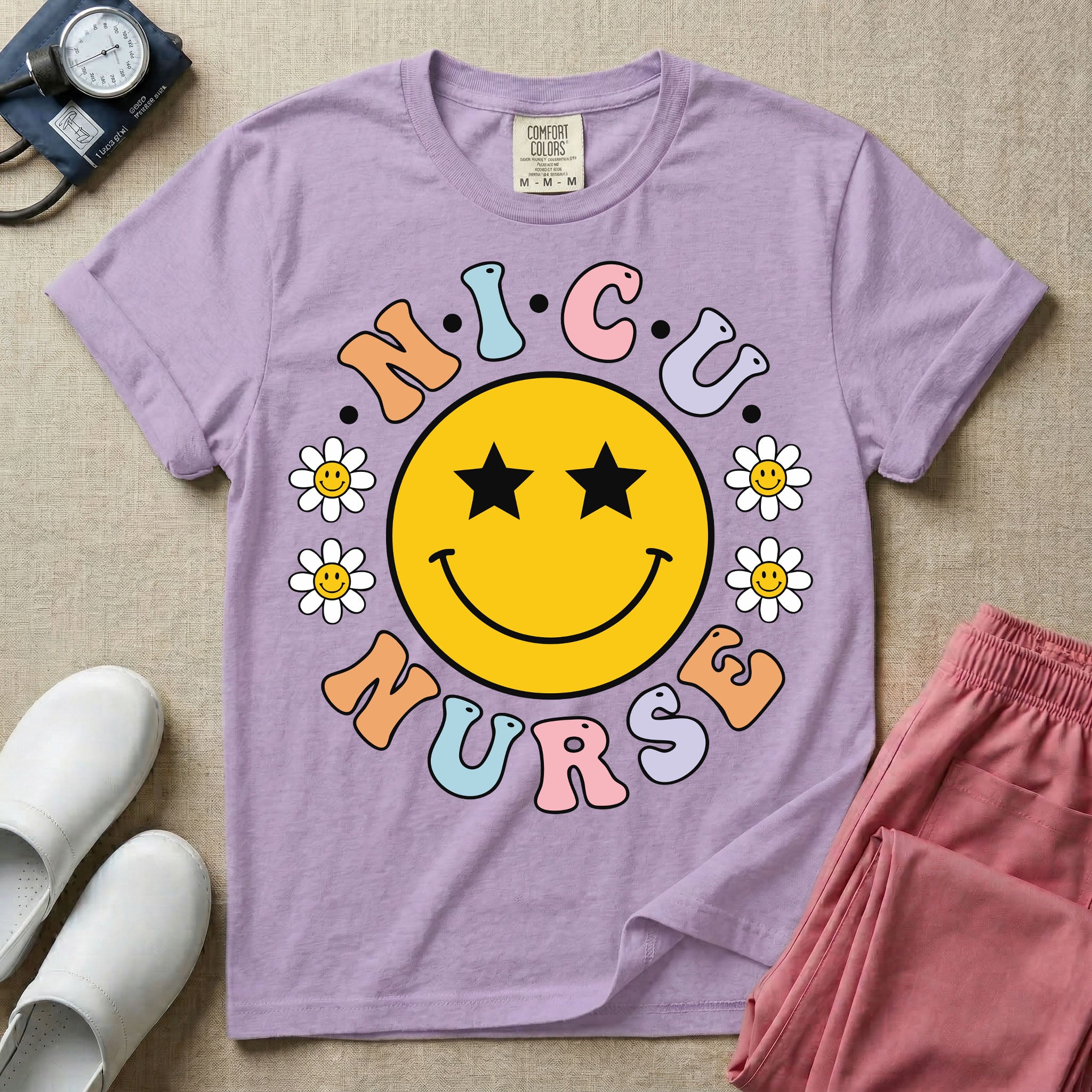 A t-shirt featuring a large yellow smiley face with star eyes surrounded by smiley face daisies and the text N.I.C.U. NURSE in pastel retro bubble lettering.