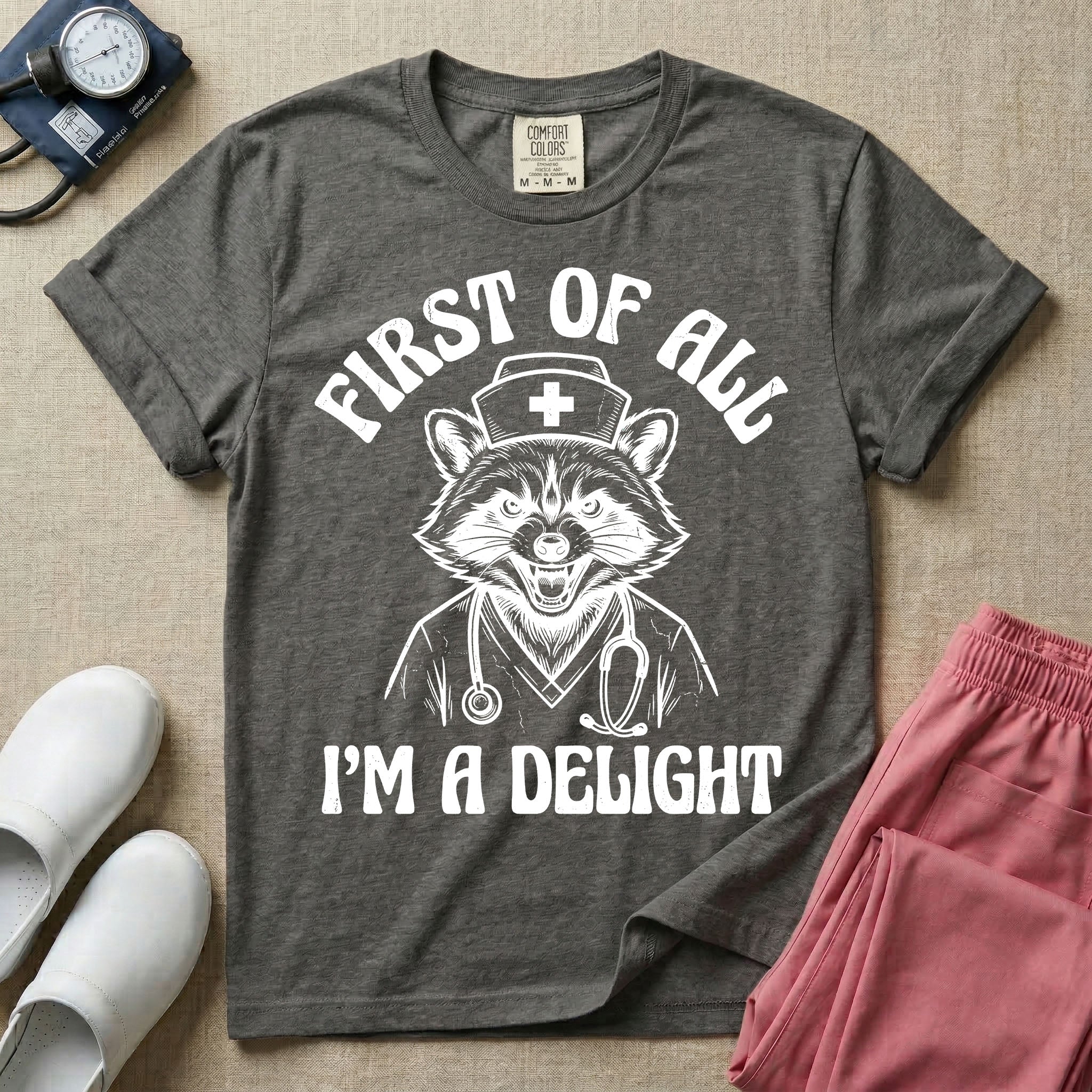 A humorous graphic of a raccoon dressed in a nursing cap and scrub jacket with a stethoscope, with the text "FIRST OF ALL I'M A DELIGHT", in pepper color.