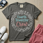 A postpartum nursing t-shirt featuring the stacked text "Fourth Trimester Crew" in blue and pink retro fonts, surrounded by a circular border of white minimalist line drawings depicting newborn and postpartum care items including a breast pump, swaddled baby, maternity bra, maxi pad, stethoscope, wipes, and a nursing pillow.