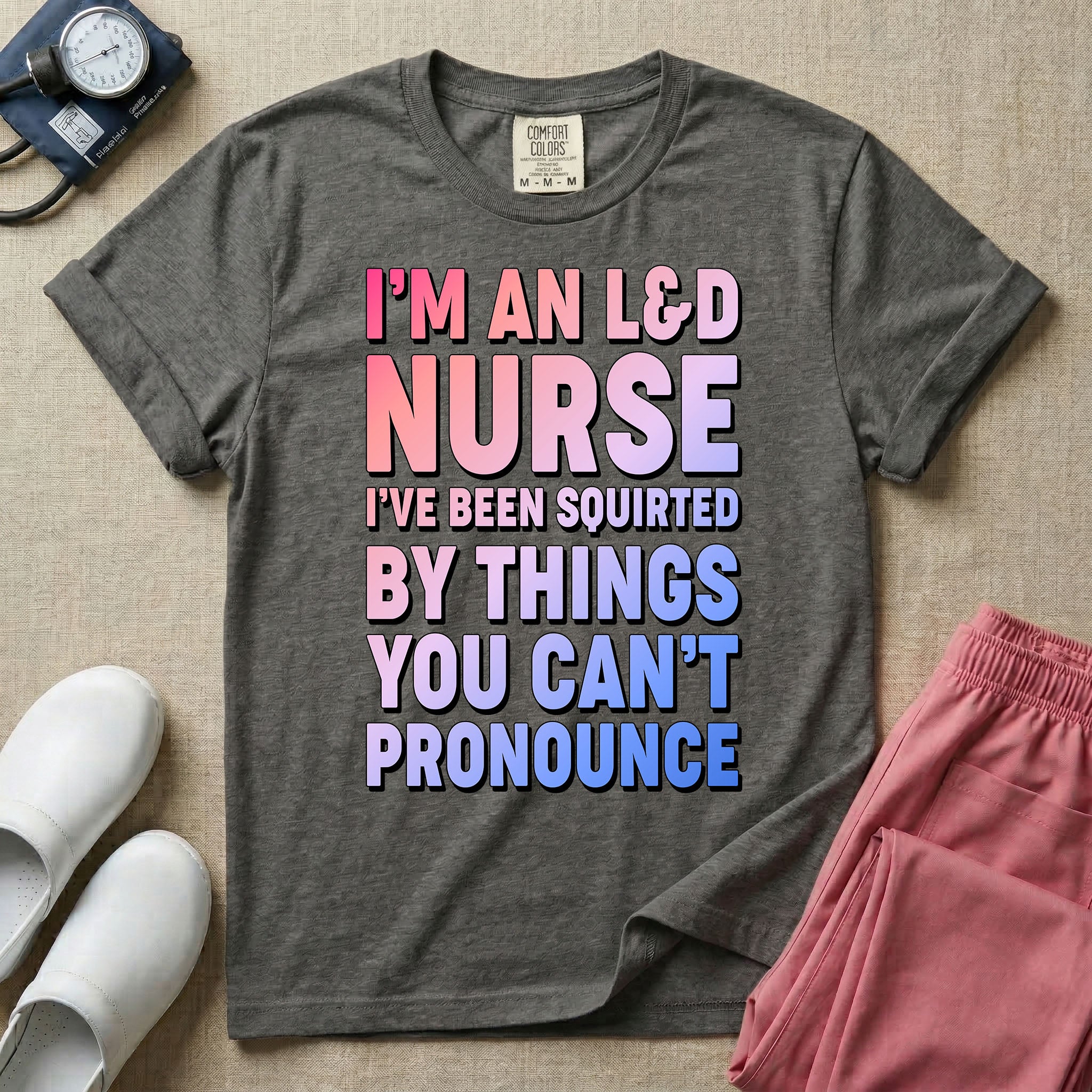 A humorous graphic tee for labor and delivery nurses featuring bold, gradient block lettering that reads "I'M AN L&D NURSE I'VE BEEN SQUIRTED BY THINGS YOU CAN'T PRONOUNCE".