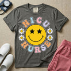A t-shirt featuring a large yellow smiley face with star eyes surrounded by smiley face daisies and the text N.I.C.U. NURSE in pastel retro bubble lettering.
