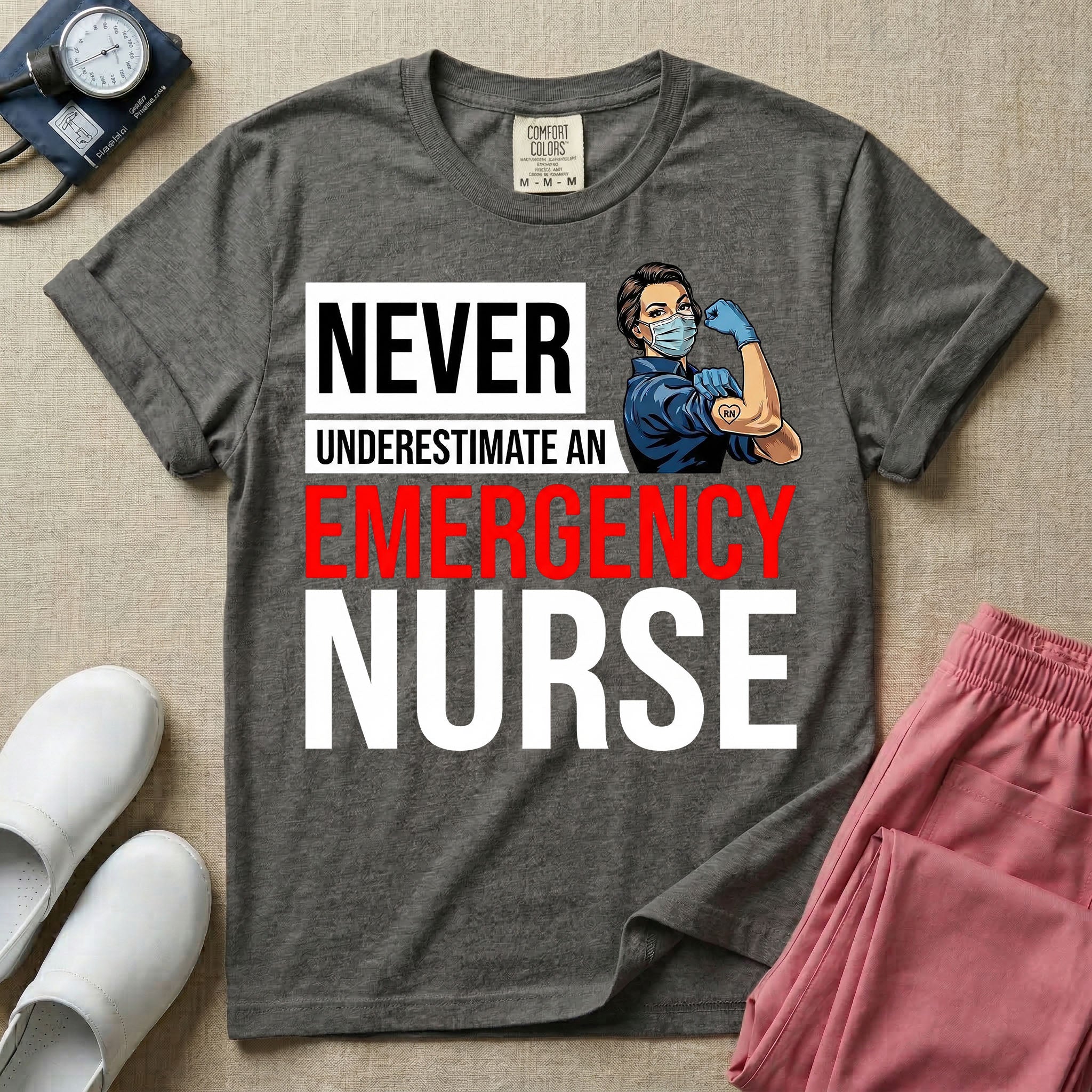 A retro ER nursing t-shirt featuring the bold text "NEVER UNDERESTIMATE AN EMERGENCY NURSE" alongside a vintage graphic of a masked nurse flexing her arm in a classic Rosie the Riveter pose
