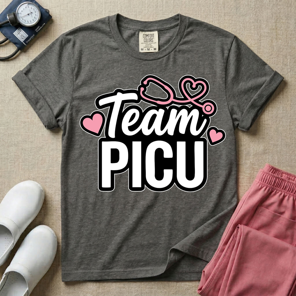 A descriptive graphic tee for pediatric intensive care nurses featuring the text "Team PICU" in bold white lettering, accented with pink hearts and a pink stethoscope design.