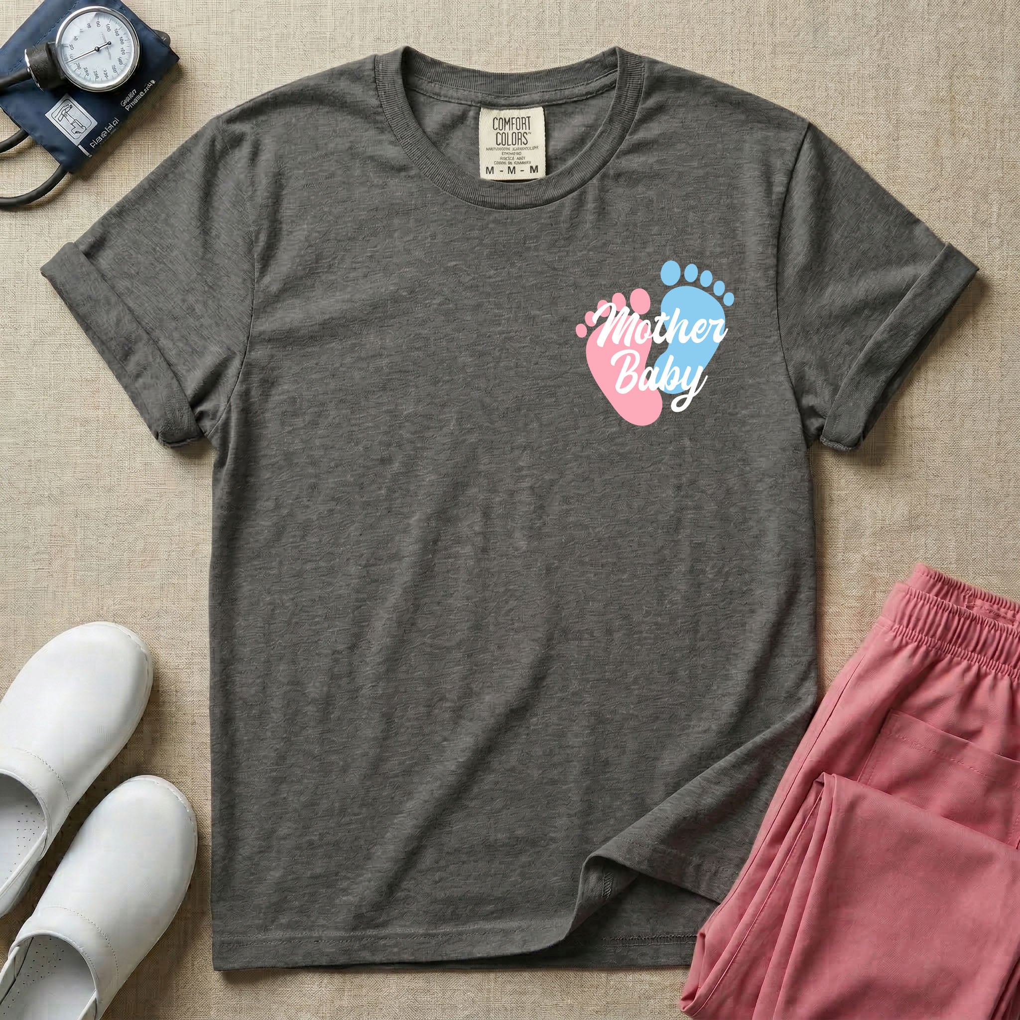 A minimalist postpartum nursing t-shirt featuring a small left chest graphic of two baby footprints, one pink and one blue, with the cursive white text "Mother Baby" written across them.