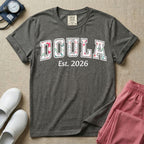 A personalized Doula graphic featuring the word DOULA in large, arched varsity-style letters filled with a delicate pink and green floral pattern, positioned above customizable text that reads Est. 2026.