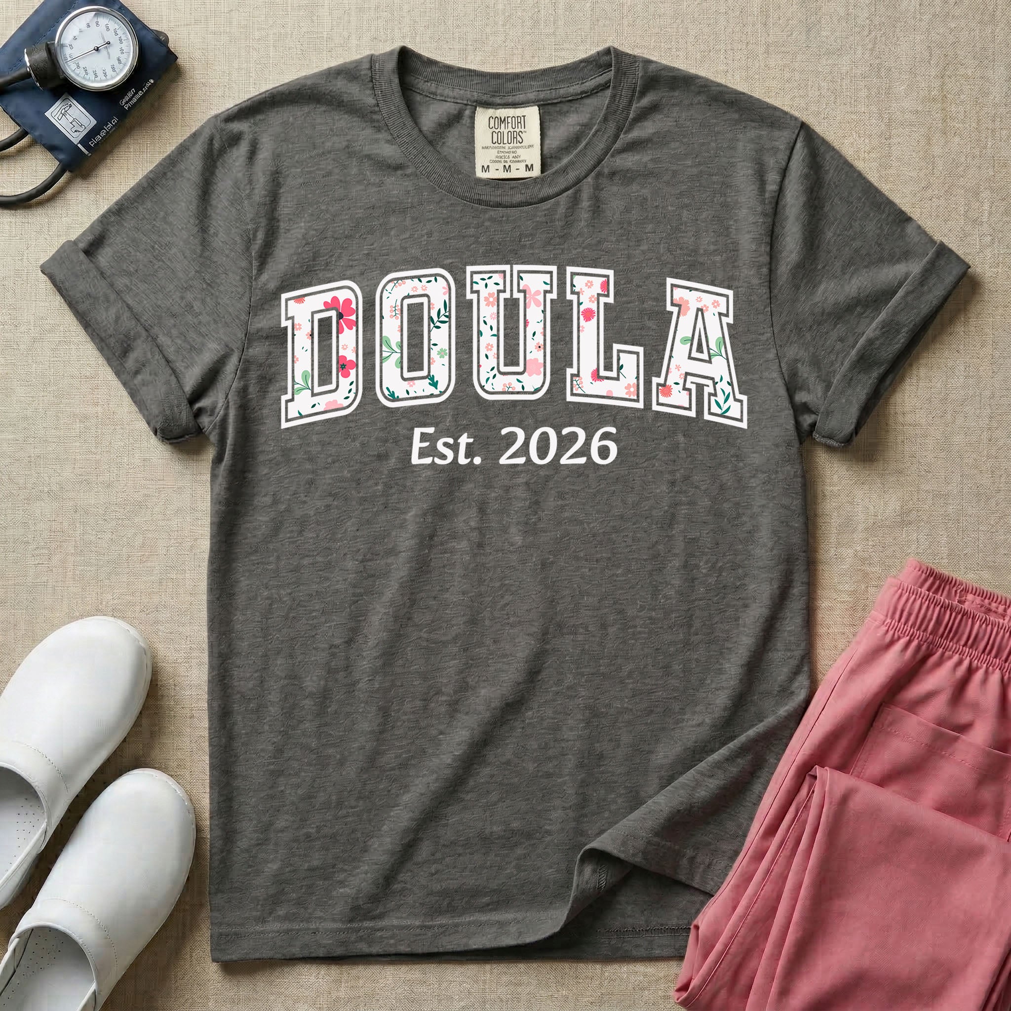 A personalized Doula graphic featuring the word DOULA in large, arched varsity-style letters filled with a delicate pink and green floral pattern, positioned above customizable text that reads Est. 2026.