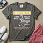 A humorous and retro graphic tee for labor and delivery nurses featuring a vintage nurse illustration alongside the text "FIELD GUIDE TO L&D", "STANCE: WIDE", "REFLEXES: SHARP", "PATIENCE: NON-EXISTENT", and "CAUTION: HIGH PROBABILITY OF UNPLANNED HYDROMASSAGE".