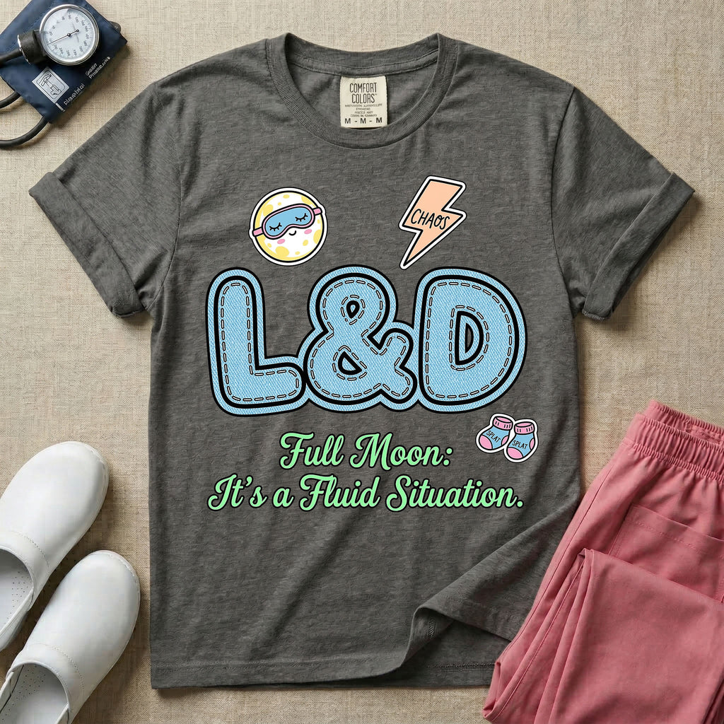 A humorous Labor and Delivery nurse graphic featuring large, light blue varsity-style letters spelling L&D with a pink dashed outline, surrounded by small patch-like icons of a baby and a lightning bolt, sitting above cursive text that reads Full Moon: It's a Fluid Situation.