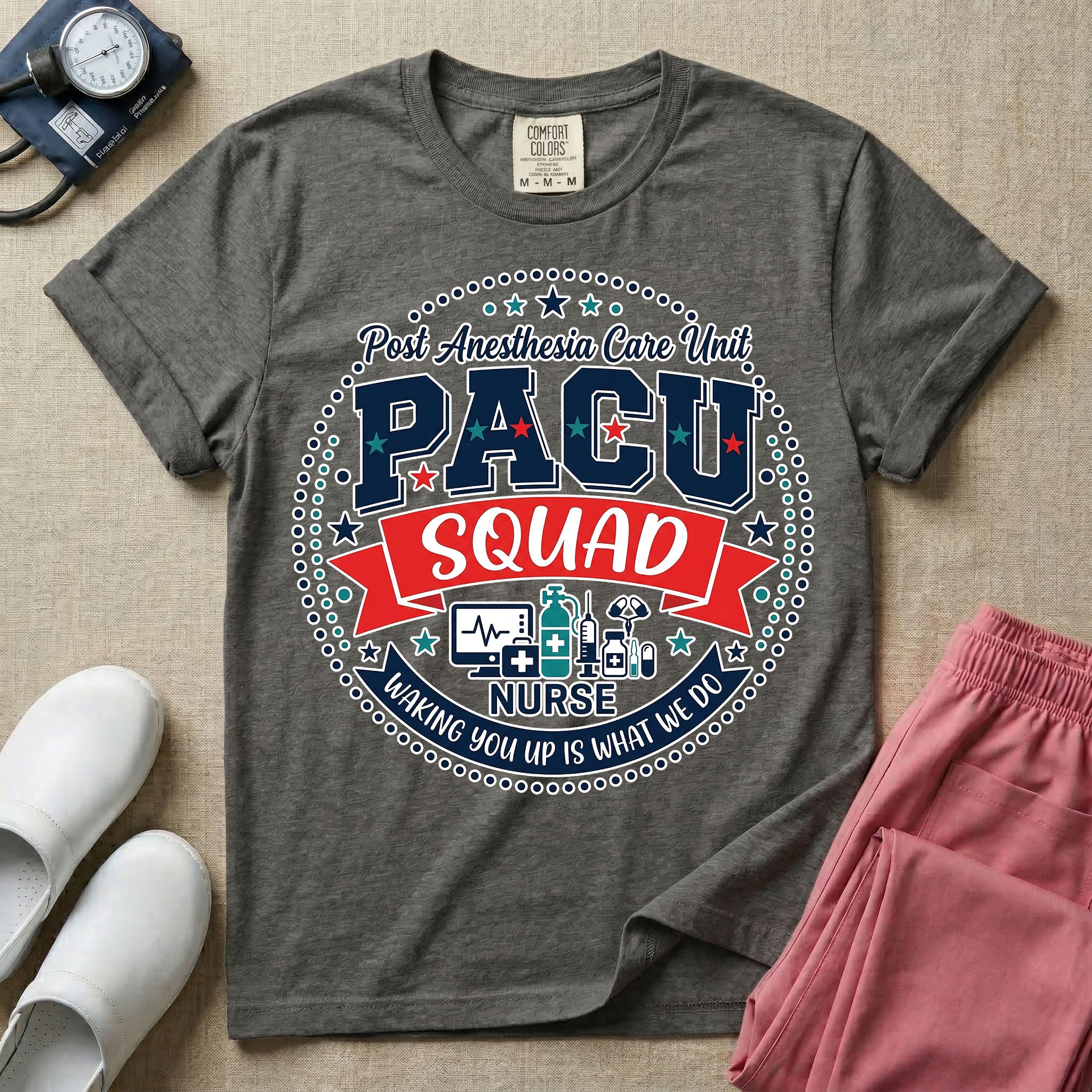 A t-shirt featuring a circular badge design with the text PACU SQUAD in block letters, medical icons like a heart monitor and stethoscope, and the phrase Waking You Up Is What We Do.