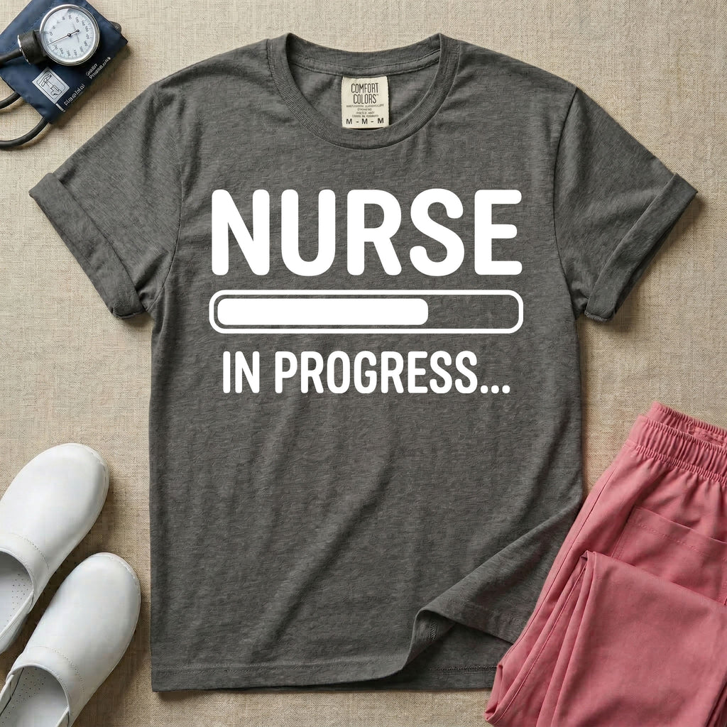 General nursing student t-shirt featuring a white loading bar graphic and the text "NURSE IN PROGRESS..." on a dark gray garment, in pepper color.