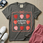A funny and cute postpartum nursing t-shirt featuring the pun text "postpartum is my jam" surrounded by a graphic of red and pink strawberries, enclosed in a decorative wavy border with a bow at the top.