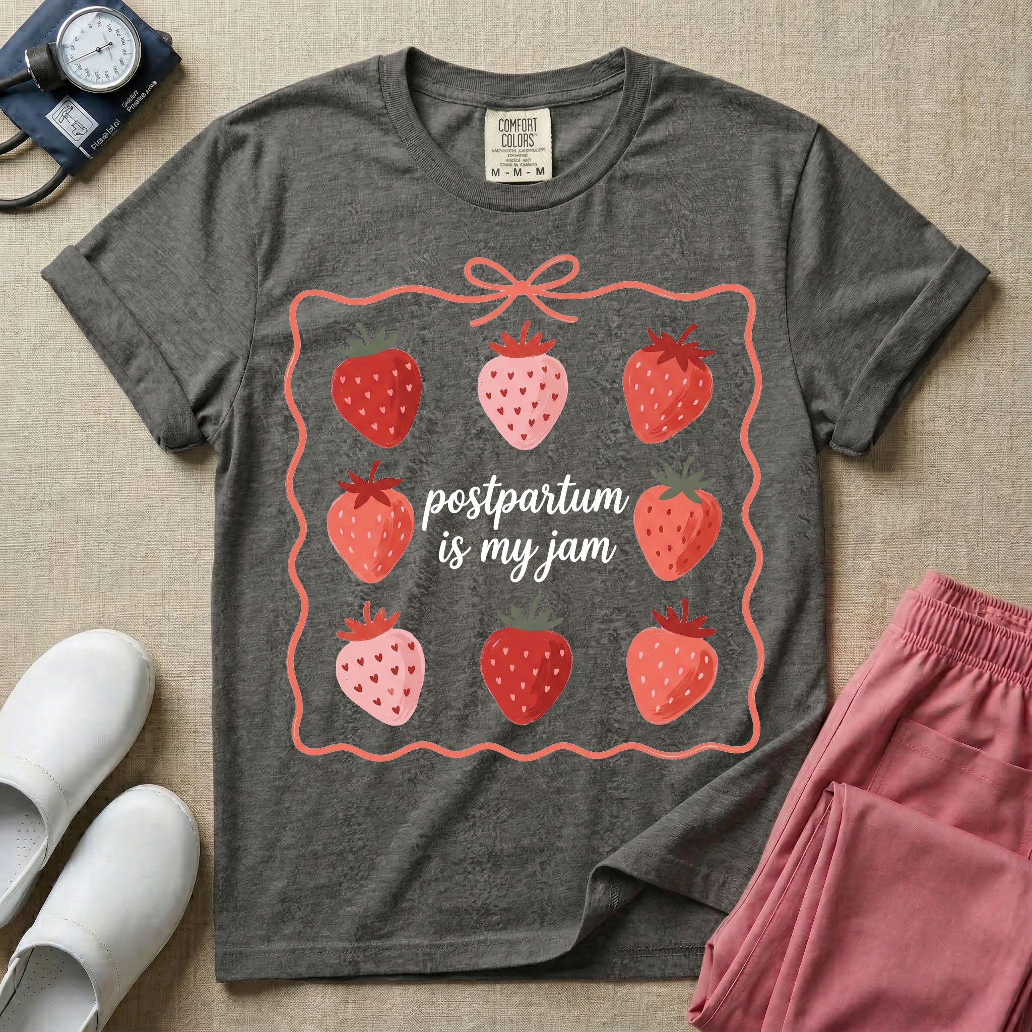 A funny and cute postpartum nursing t-shirt featuring the pun text "postpartum is my jam" surrounded by a graphic of red and pink strawberries, enclosed in a decorative wavy border with a bow at the top.