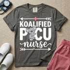A funny pediatric intensive care nursing t-shirt featuring the pun text "KOALIFIED PICU nurse" with a cute koala graphic replacing the letter I in PICU, framed by decorative arrows and a pink medical cross.