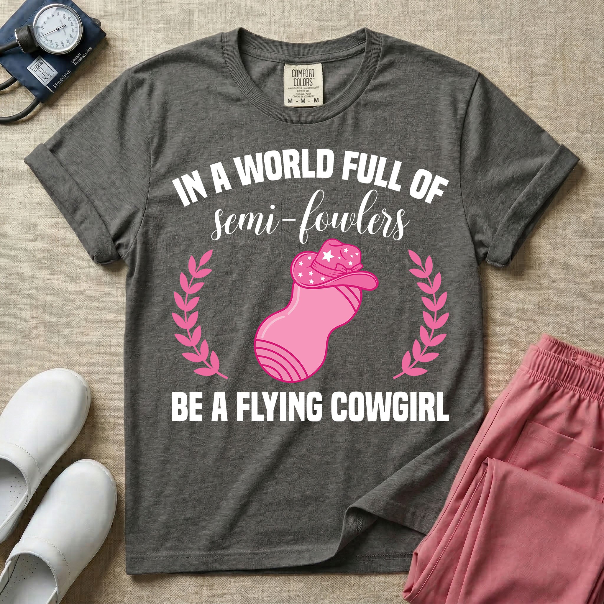 A humorous graphic tee for labor and delivery nurses featuring an illustration of a peanut ball wearing a cowboy hat, framed by laurel branches, along with the text "IN A WORLD FULL OF semi-fowlers BE A FLYING COWGIRL".