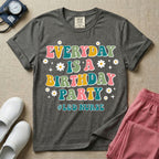 A retro graphic tee for labor and delivery nurses featuring bubble lettering that reads "EVERYDAY IS A BIRTHDAY PARTY #L&D NURSE" surrounded by small daisies and stars.