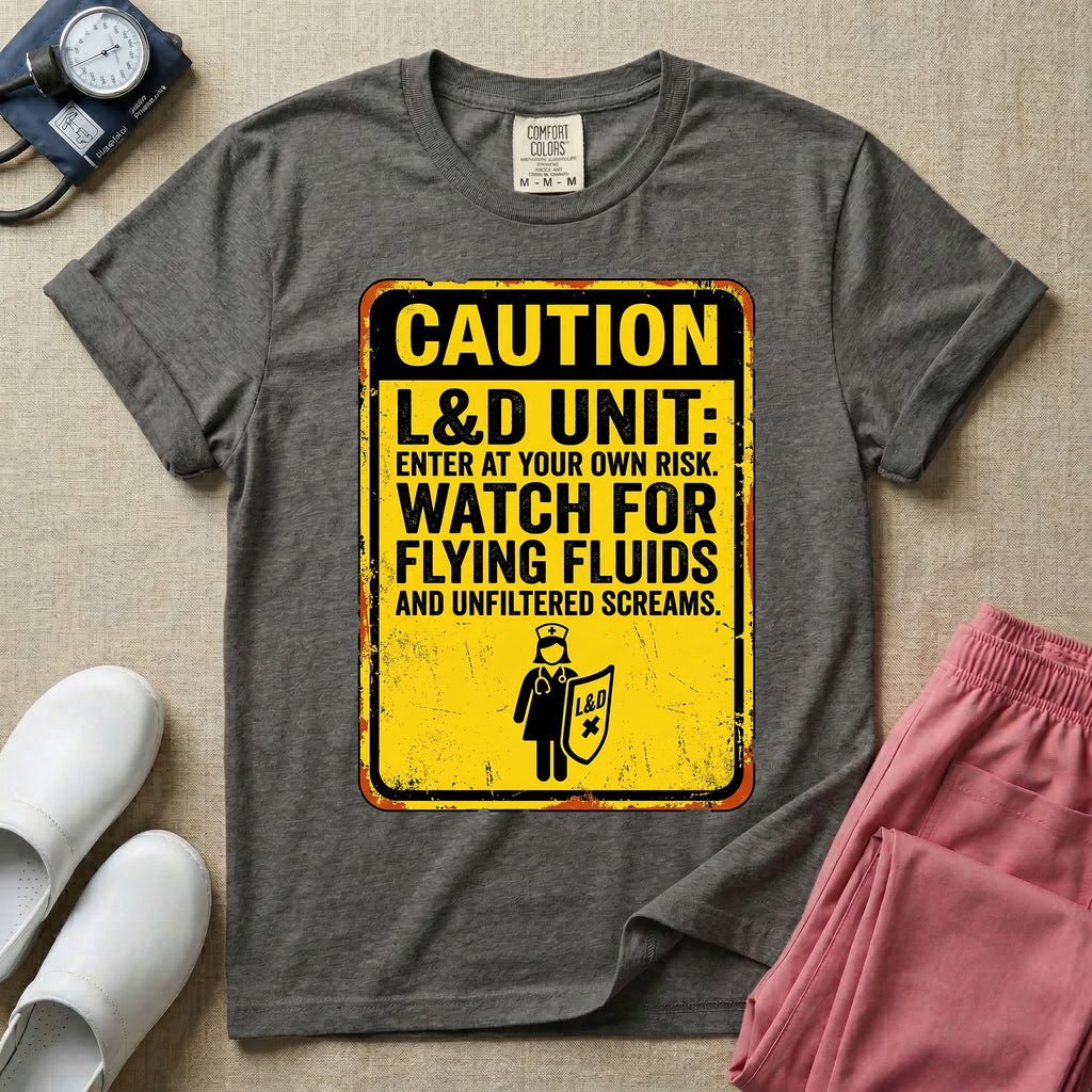 A humorous graphic tee for labor and delivery nurses featuring a distressed caution sign design with the text "CAUTION L&D UNIT: ENTER AT YOUR OWN RISK. WATCH FOR FLYING FLUIDS AND UNFILTERED SCREAMS." above a stick figure nurse holding a shield.