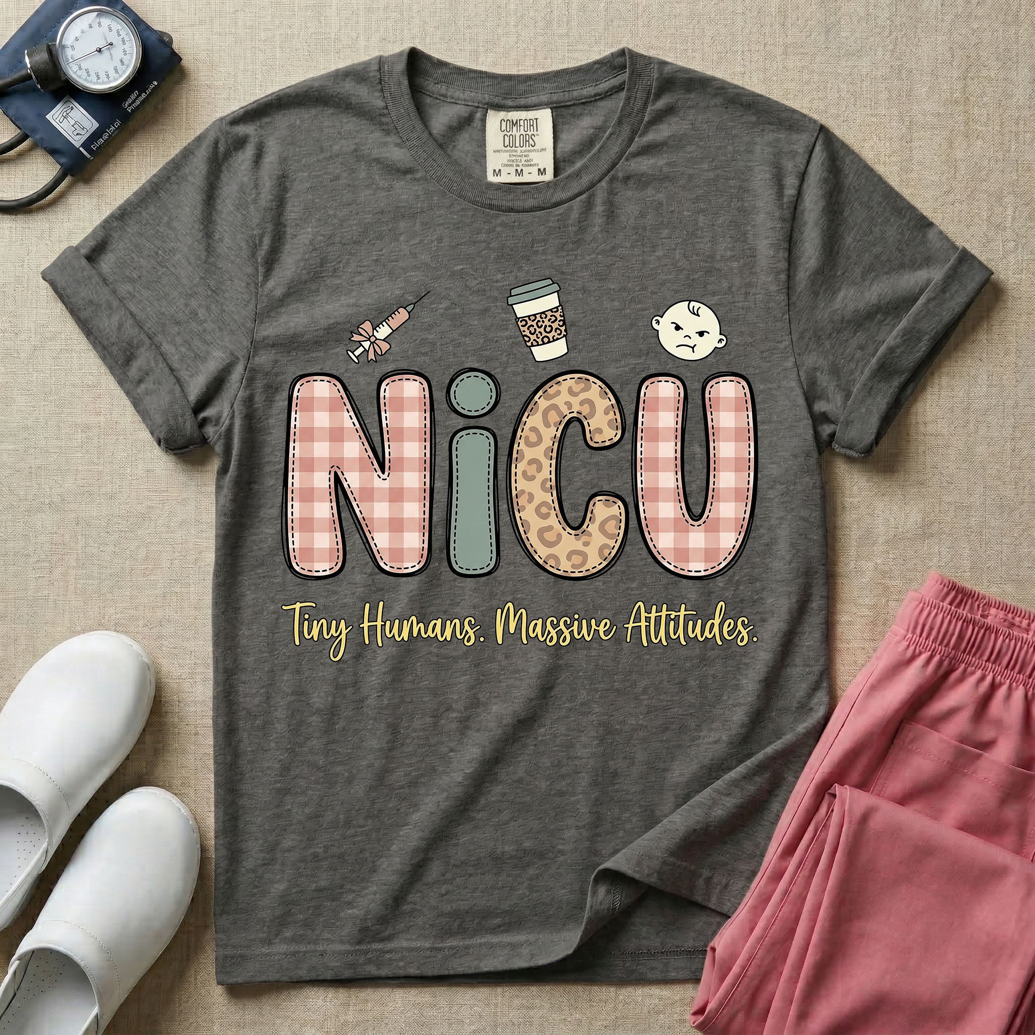 A humorous t-shirt for NICU nurses featuring the large text "NICU" in plaid and patterned letters with the phrase "Tiny Humans. Massive Attitudes." underneath, accompanied by small cute graphics of a syringe, an iced coffee cup, and a baby's face.